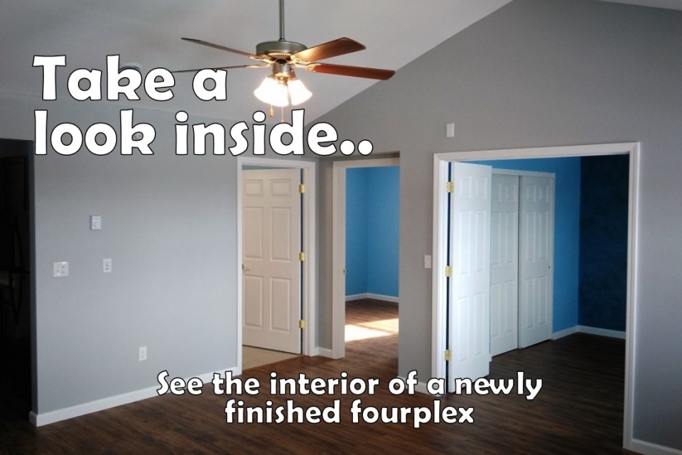 Image of a fourplex unit interior living room with gray blue walls and dark wood floors. Text reads "Take a look inside. See the interior of a newly finished fourplex."